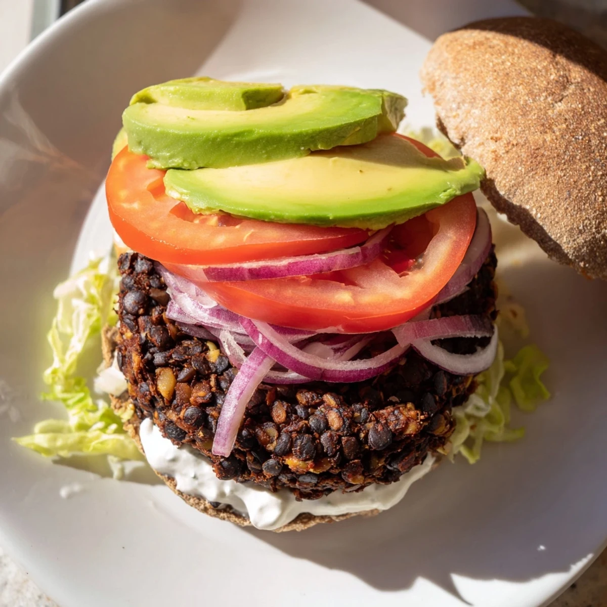 Close-up of a stacked Zesty Weeknight Black Bean Burger, showcasing fresh avocado and vibrant toppings.