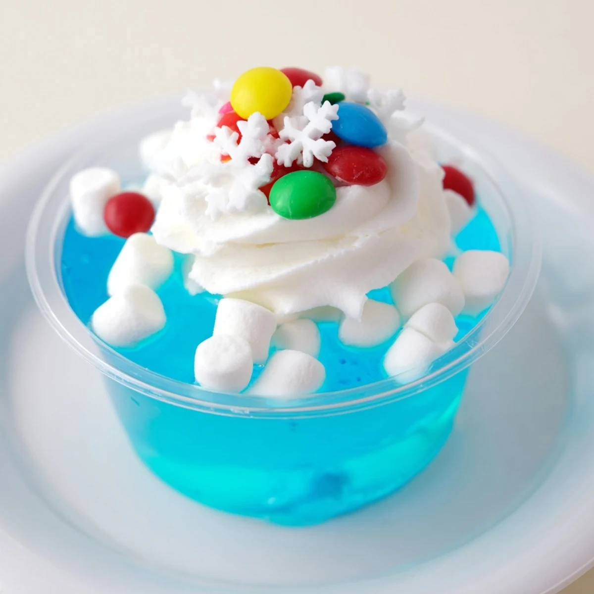 Vibrant blue snow globe Jello cups, layered with marshmallows and sprinkles, a festive dessert.