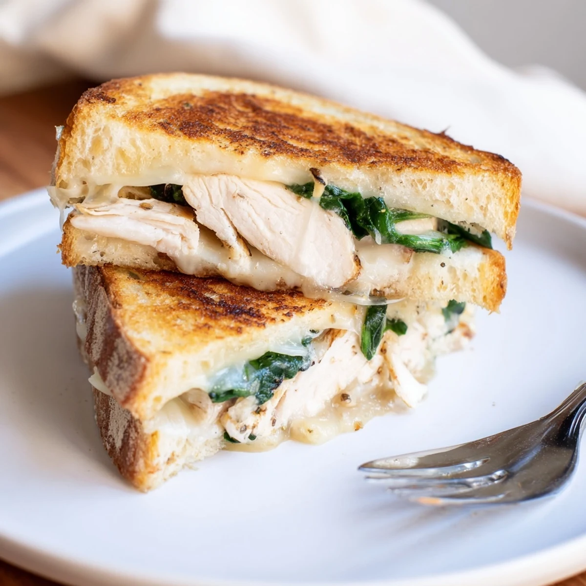 Golden-brown Grilled Chicken Spinach Panini sliced in half, revealing layers of juicy chicken, fresh spinach, and melted mozzarella cheese on crusty bread.