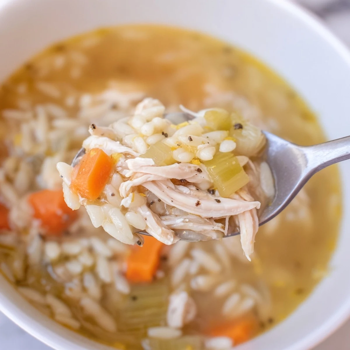 Golden-hued Lemon Pepper Chicken Orzo Soup steams in a white bowl, garnished with fresh parsley and lemon wedges.