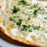 A slice of Creamy Garlic White Pizza lifted to reveal its velvety garlic sauce, melted cheese, and golden baked crust.