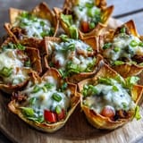 Crispy wonton taco cups topped with melted cheese and fresh garnishes.