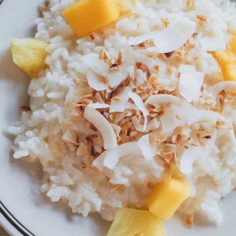Warm Coconut Rice Sweet topped with toasted coconut flakes and fresh mango on a white plate.  
