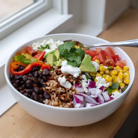 Warm brown rice burrito bowl layered with black beans, colorful bell peppers, corn, tomatoes, red onion, and fresh avocado slices.  