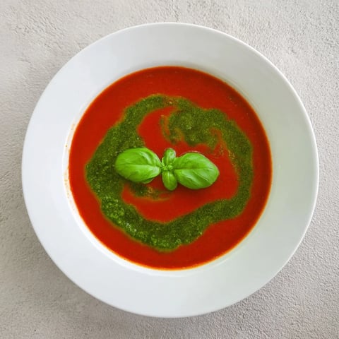 Creamy tomato soup with basil pesto swirl served warm in a white bowl with crusty bread.