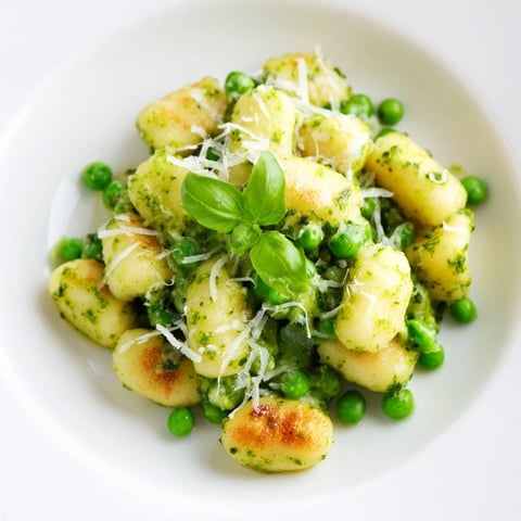 Golden, crispy pan-fried gnocchi tossed with vibrant green peas and fresh basil pesto in a skillet.  
