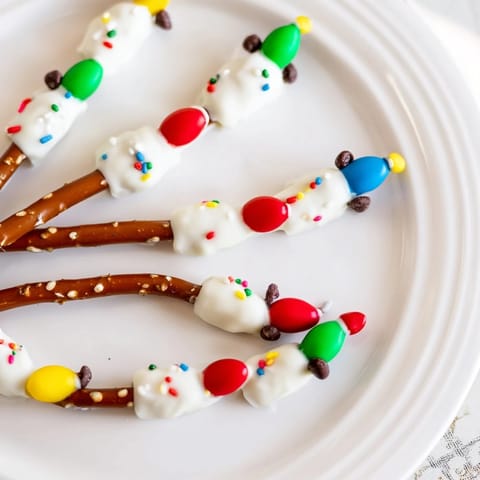 No-bake pretzel sticks Christmas lights feature dipped pretzels with colorful candy bulbs, chocolate wires, and festive sprinkles.