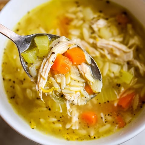 A spoon dips into savory Lemon Pepper Chicken Orzo Soup, revealing tender shredded chicken and orzo in bright broth.