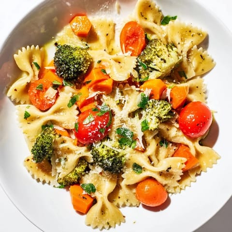 A close-up view of a colorful serving of rainbow veggie pasta primavera garnished with basil and Parmesan on a rustic table.