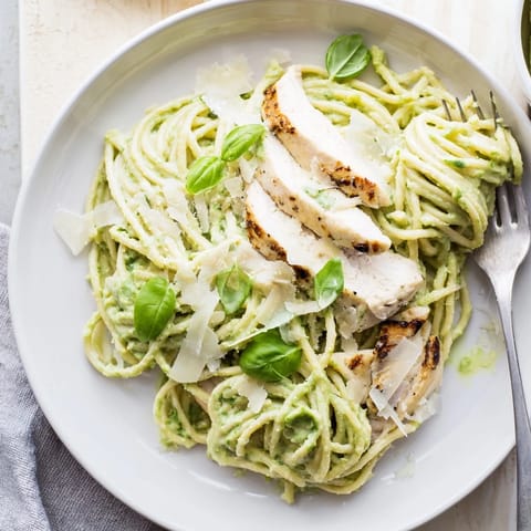 A close-up of Creamy Avocado Chicken Pasta with fresh basil leaves, lemon zest, and a light drizzle of extra virgin olive oil.