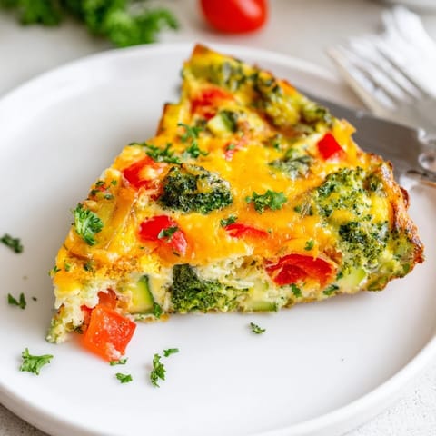 Colorful slice of vegetable frittata featuring zucchini, red onion, and herbs, served with a fresh side salad.