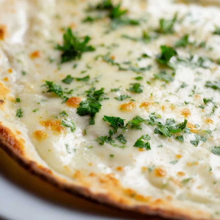A slice of Creamy Garlic White Pizza lifted to reveal its velvety garlic sauce, melted cheese, and golden baked crust.