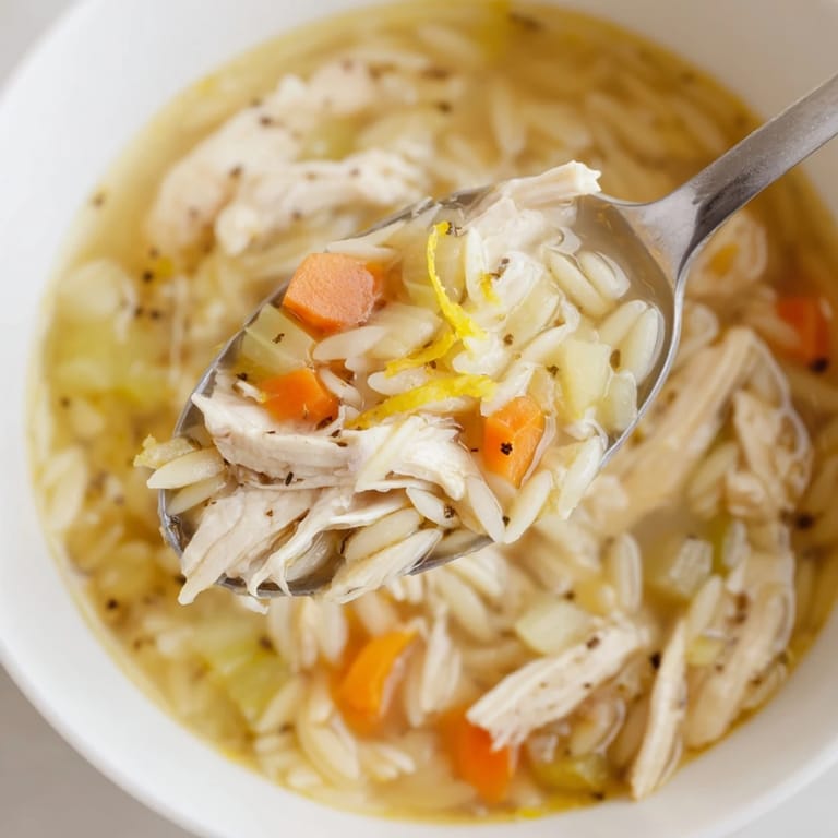 Close-up of steaming Lemon Pepper Chicken Orzo Soup in a rustic bowl, topped with parsley and Parmesan cheese.