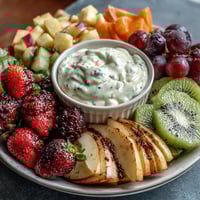 Vibrant spring fruit platter with strawberries, kiwi, and pineapple, served with creamy honey-yogurt dipping sauce for a refreshing snack.