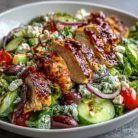 A colorful Greek salad bowl topped with tender grilled chicken, fresh vegetables, and creamy feta, drizzled with zesty lemon dressing.  