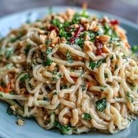 A colorful Thai peanut noodle salad with fresh vegetables, herbs, and creamy lime-peanut dressing in a white bowl.  